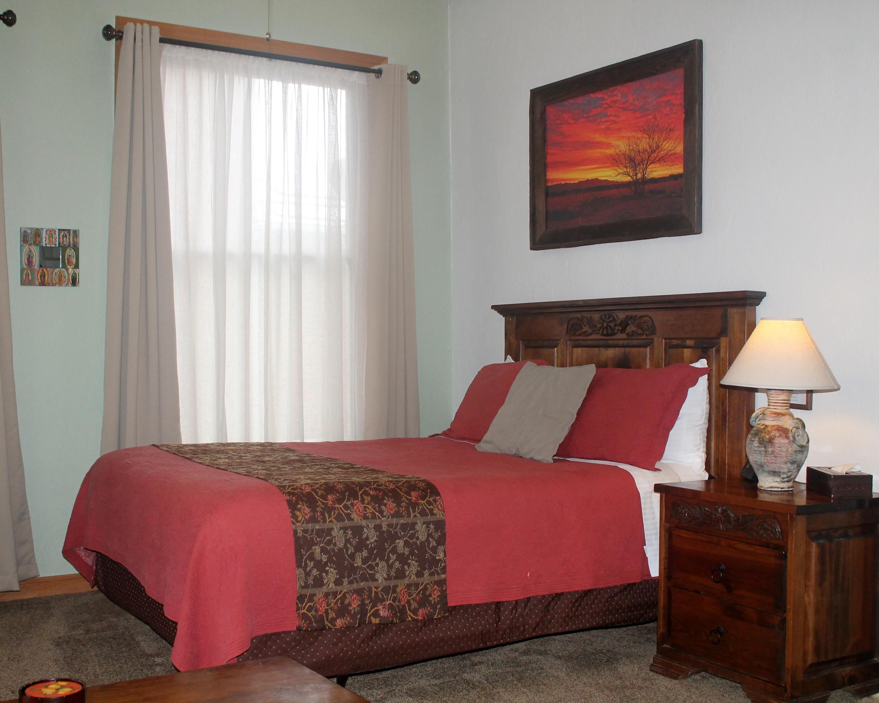 Canyon Rose Suites in Bisbee bedroom with red bedspread, nightstand lamp, and framed sunset art.