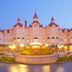 Disneyland Hotel in Chessy at dusk, featuring a grand fairytale facade and flower garden with lit fountain