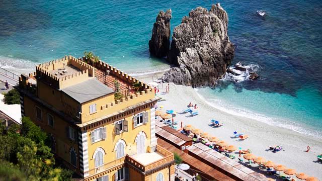 Hotel Meublè Agavi in Monterosso al Mare overlooks a beach with umbrellas and a rocky sea stack.