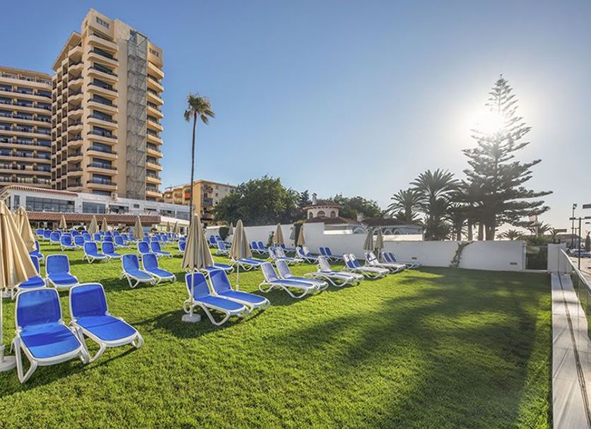 Globales Gardenia in Fuengirola: sunlit lawn with blue lounge chairs and umbrellas by the hotel