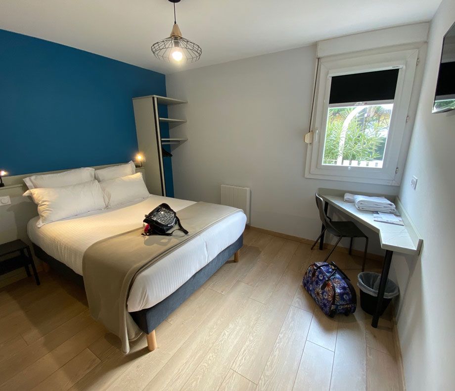 Hôtel Azur in Agde guest room with double bed, desk by window, and blue accent wall