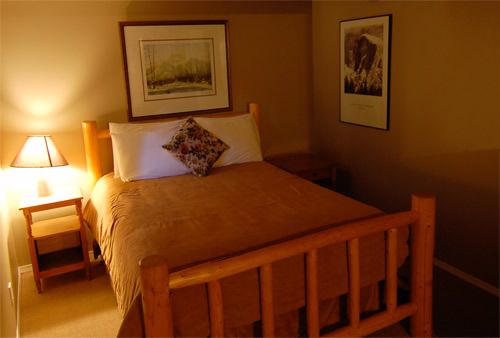 Charlie's Guesthouse in Field: cozy guest room with wooden bed, bedside lamp, and framed wall art