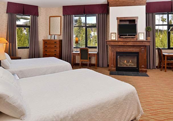 The Lodge at Big Sky guest room with two beds, fireplace, and mountain-view windows in Big Sky