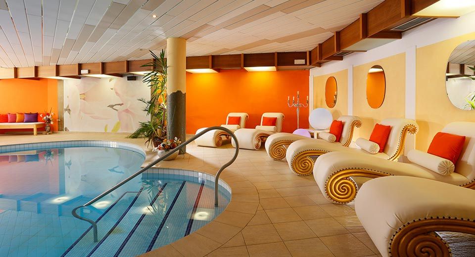 Hotel Nocturnes in Naturno indoor pool with orange lounge chairs and curved tiled seating area