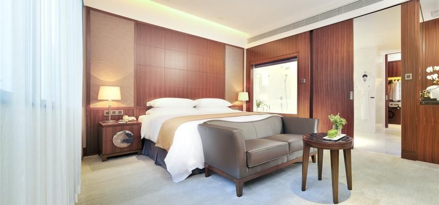 Shenzhen Nanshan L'Hermitage guest room with bed, sofa, side table, and warm wood-paneled walls in Shenzhen