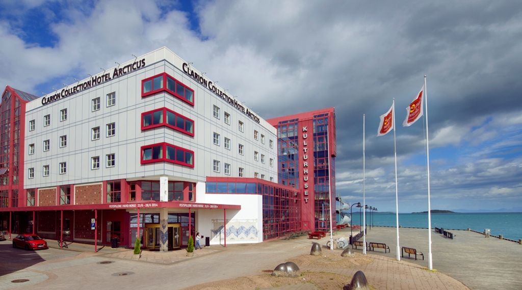 Home Hotel Arcticus in Harstad with red-trimmed facade beside a beach and calm sea