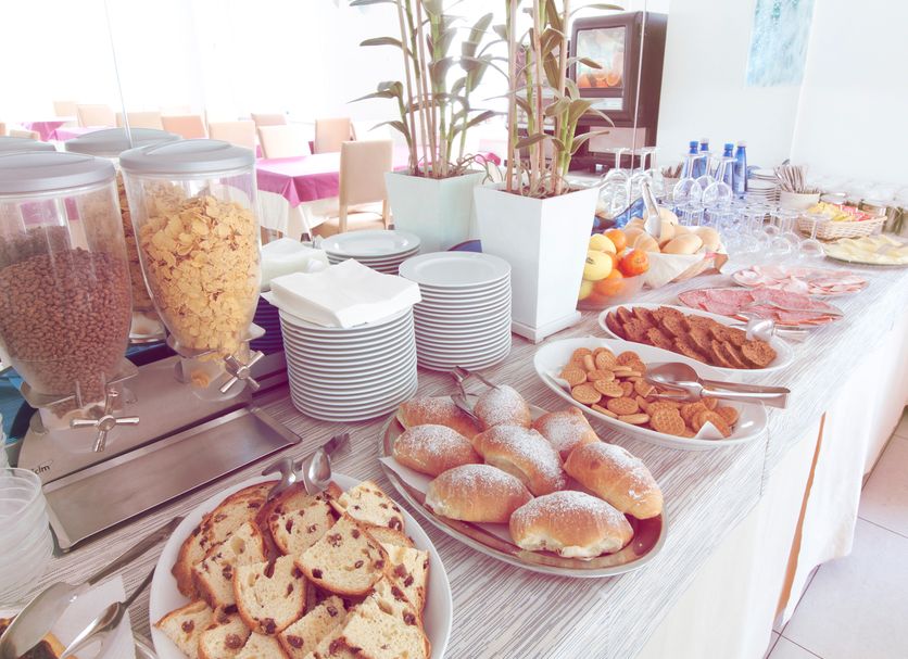 Hotel Aria di Mare in Riccione breakfast buffet with pastries, cereal dispensers and stacked plates