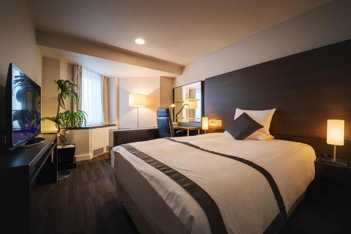 Air Terminal Hotel in Chitose guest room with king bed, desk, TV, lamp, and window seating