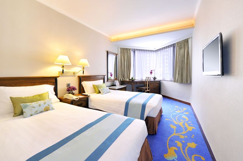 The Kimberley Hotel Hong Kong twin guest room with two beds, desk by window, and patterned blue carpet