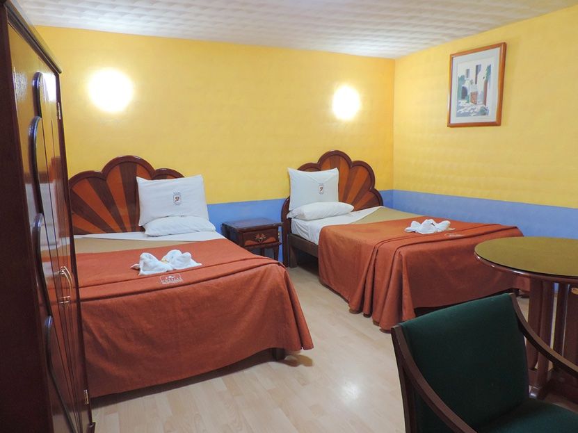 Hotel Real Tlaxcala room with two twin beds, yellow walls, and a small table in Tlaxcala